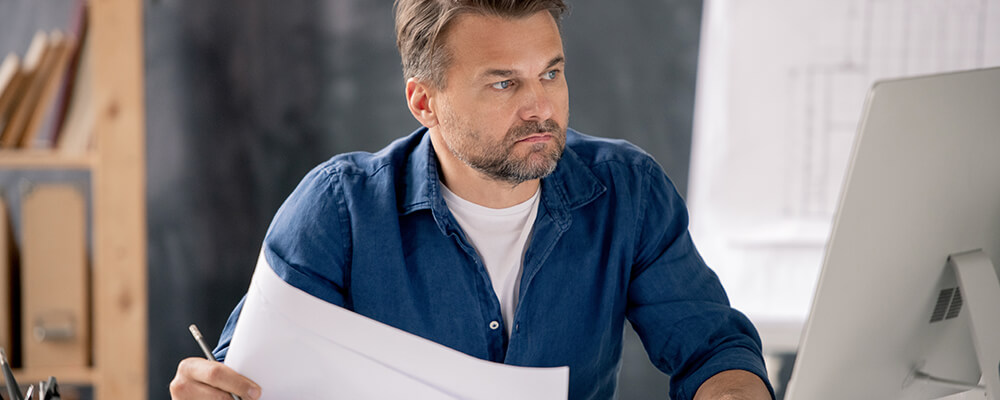 man-working-at-desk-with-computer-and-paperwork